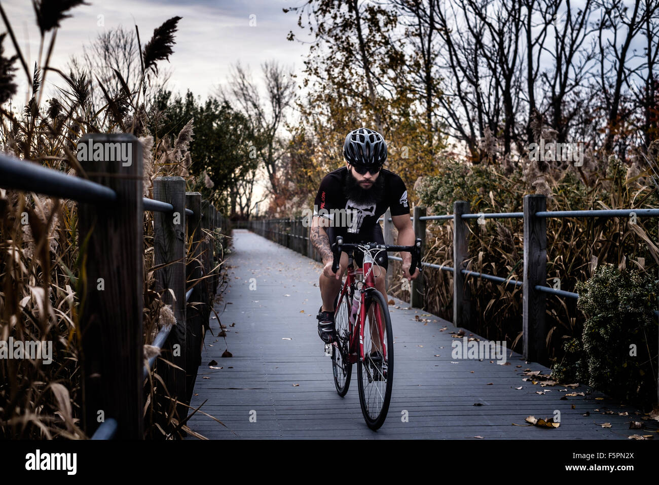 Homme barbu assis sur un vélo de route avec les mains dans les gouttes sur un pont de bois. Banque D'Images