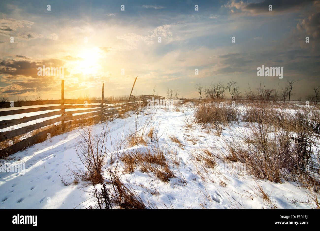 Clôture en bois en hiver, au coucher du soleil sur le terrain Banque D'Images