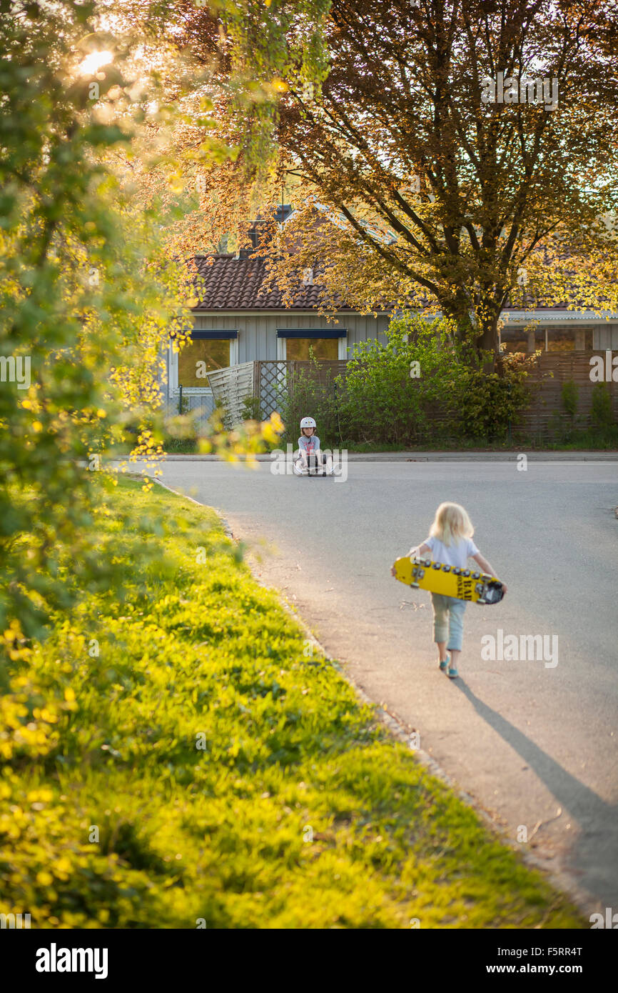 La Suède, Vastergotland, Lerum, Girl (6-7) walking to boy (8-9) avec skateboard Banque D'Images