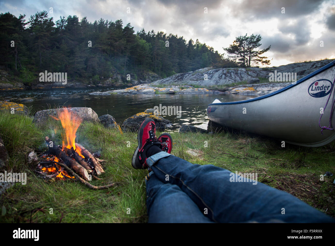 La Suède, côte ouest, Bohuslan, Flato, point de vue personnel de l'homme étendu par feu de camp on riverbank Banque D'Images