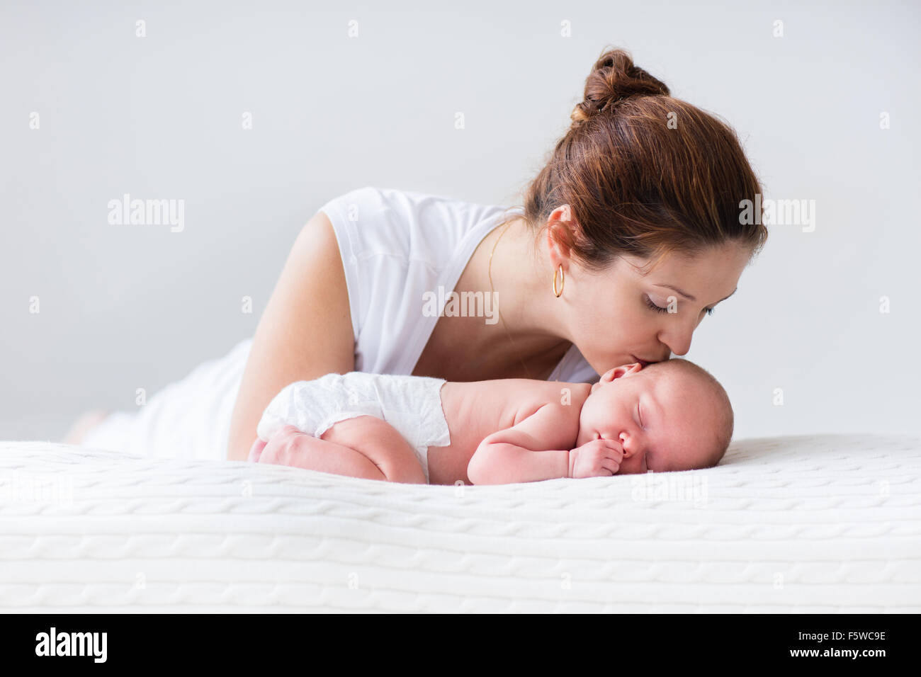 Young mother hugging son enfant nouveau-né. Maman Bébé. Femme et nouveau né garçon vous détendre dans une chambre blanche. Famille à la maison. Banque D'Images