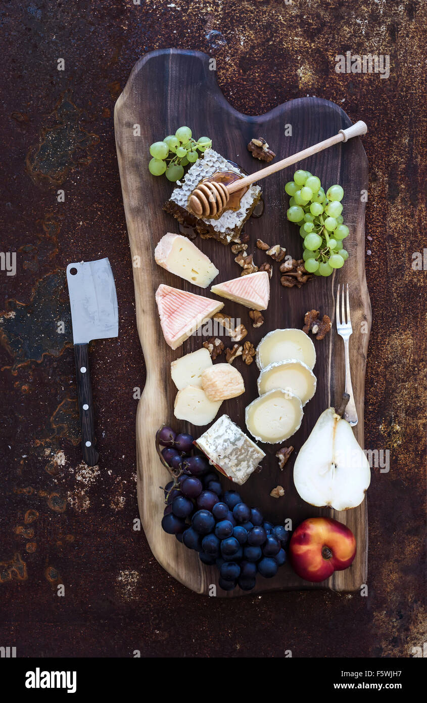 Apéritif vin set : sélection de fromages français, de miel, de raisin, de pêche et de noix sur planche de bois rustique sur dark grunge metal Banque D'Images