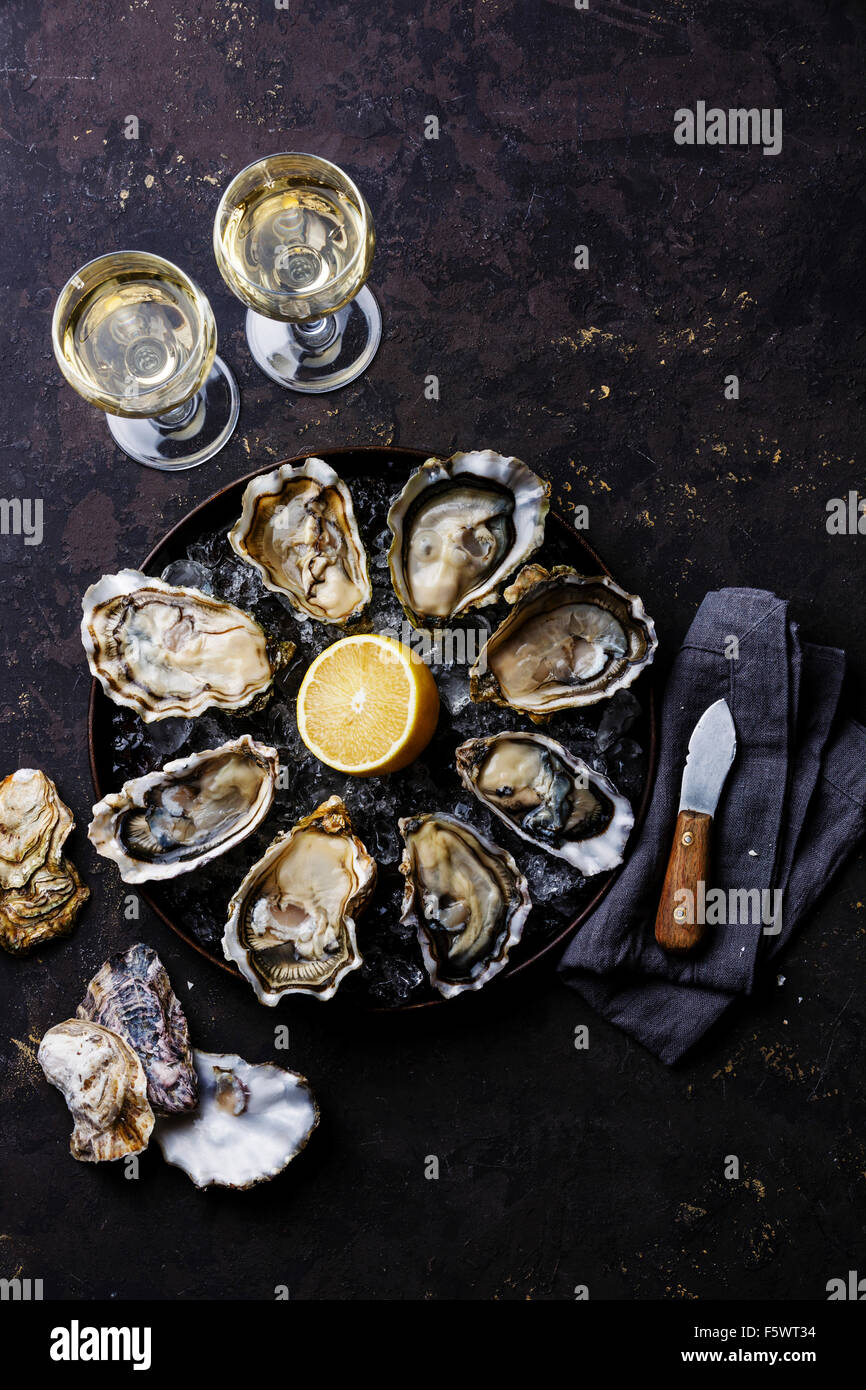 Les huîtres ouvertes speciale de claire sur la plaque et le vin blanc sur noir foncé stone texture background Banque D'Images