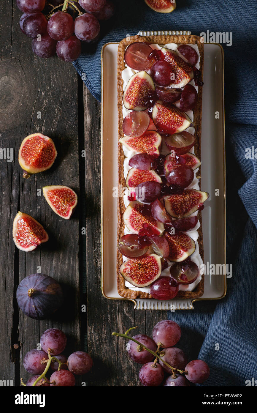 Tarte rectangulaire rouge avec des raisins, figues et à la crème fouettée dans la plaque en céramique blanche ancienne table en bois avec dessus textile bleu Banque D'Images