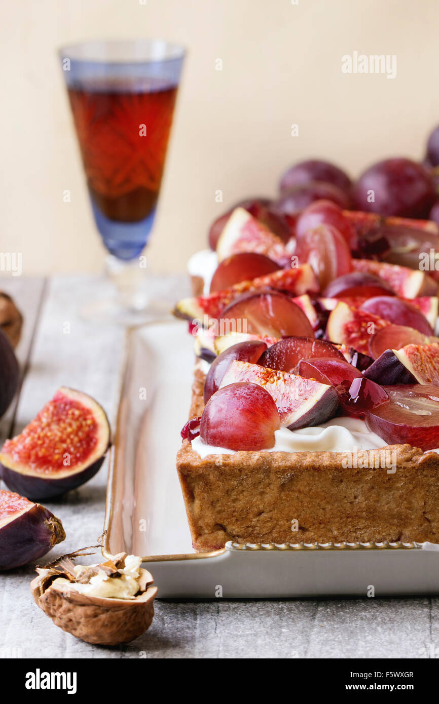 Tarte rectangulaire rouge avec des raisins, figues, noix et crème fouettée dans une plaque en céramique blanche sur table en bois blanc. Avec Banque D'Images