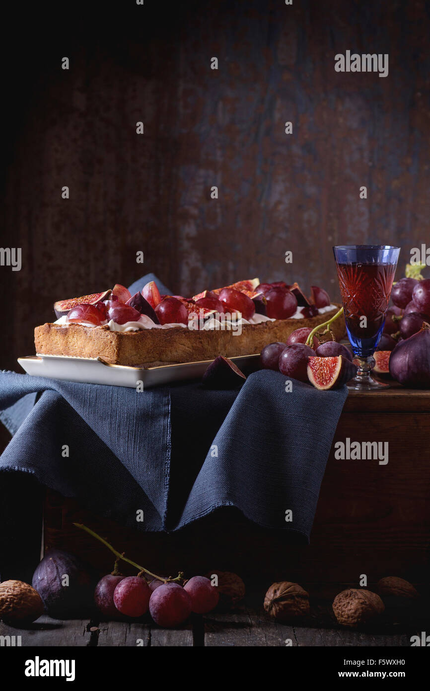 Tarte rectangulaire rouge avec des raisins, figues, noix et crème fouettée dans la plaque en céramique blanche sur la poitrine en bois plus vieux woode Banque D'Images