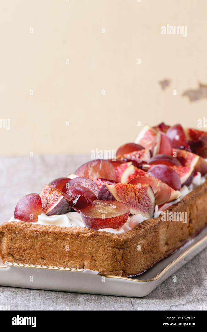 Close up de tarte rectangulaire rouge avec raisins, figues et à la crème fouettée dans la plaque en céramique blanche sur table en bois blanc. Banque D'Images