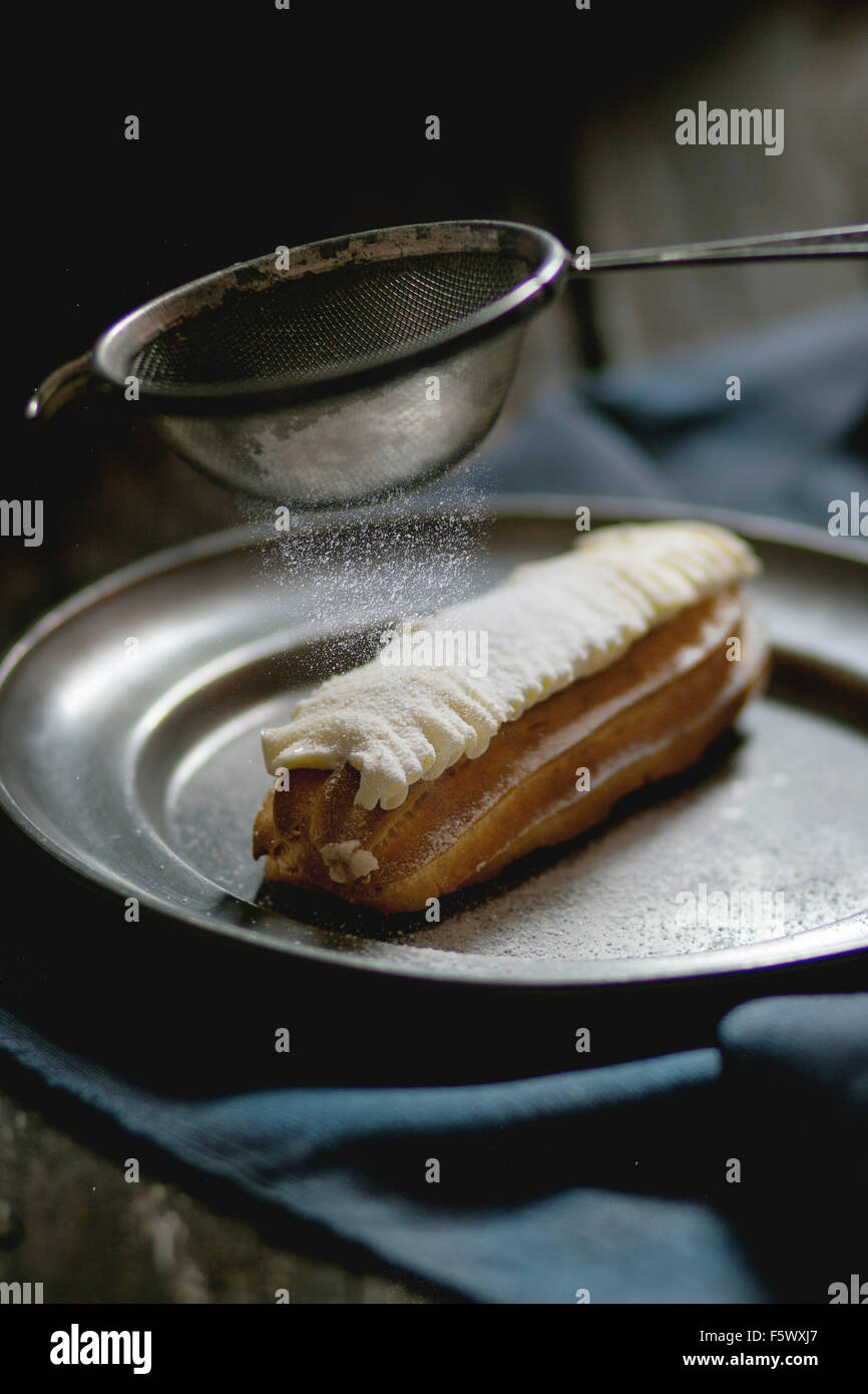 Seul Eclair avec crème au beurre blanc vintage en plaque de métal avec du sucre en poudre de tamisage. Style rustique foncé. La lumière du jour. En dehors de vi Banque D'Images