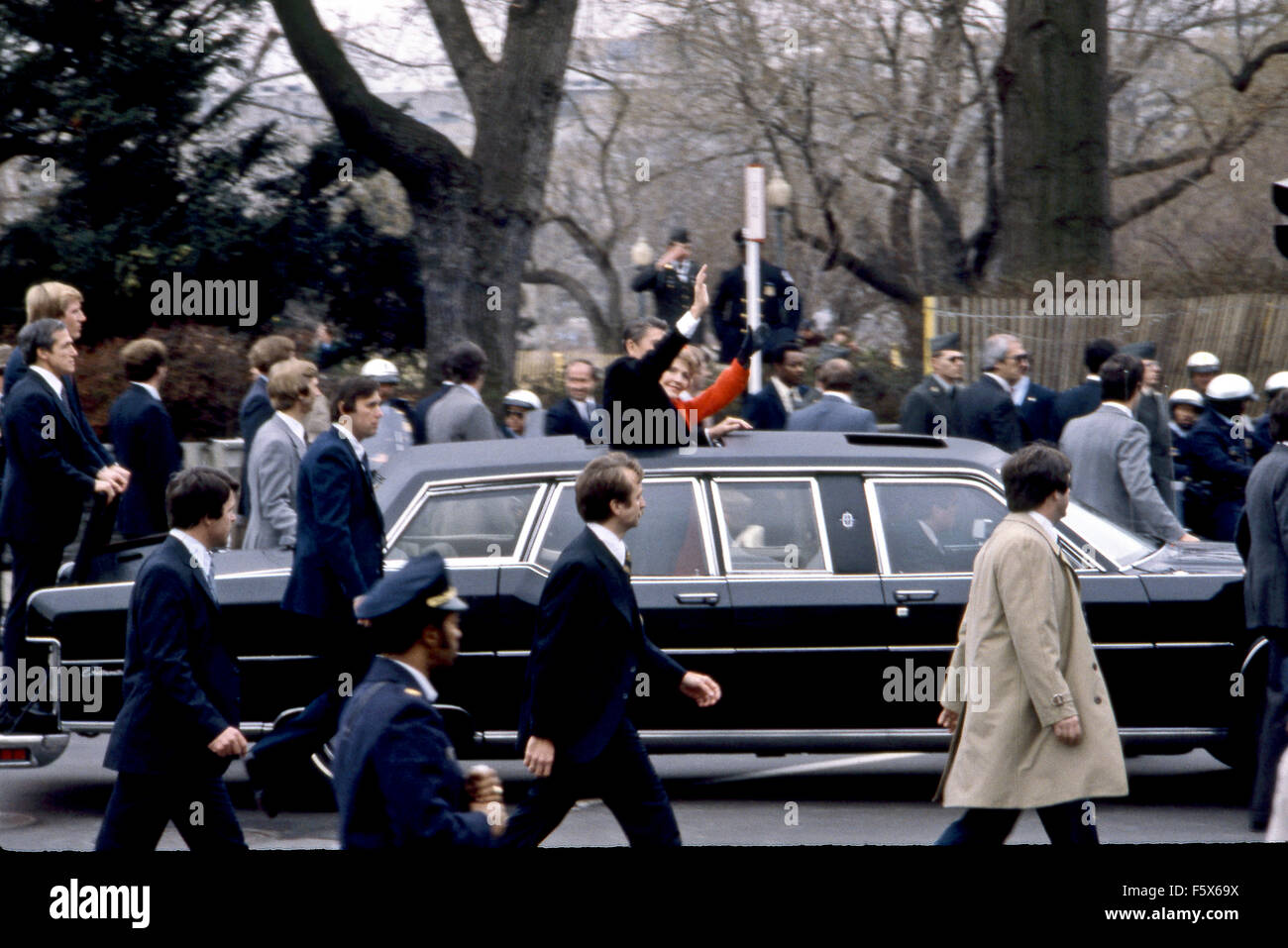 Washington, DC. USA 20 janvier 1981 Le président Ronald Reagan et Première dame Nancy Reagan vague à la foule qui tapissent le défilé inaugural du soleil toit de leur limousine. Leur détail d'agents des services secrets à pied le long de la limousine qu'il quitte le Capitole, en route vers la Maison Blanche. Banque D'Images