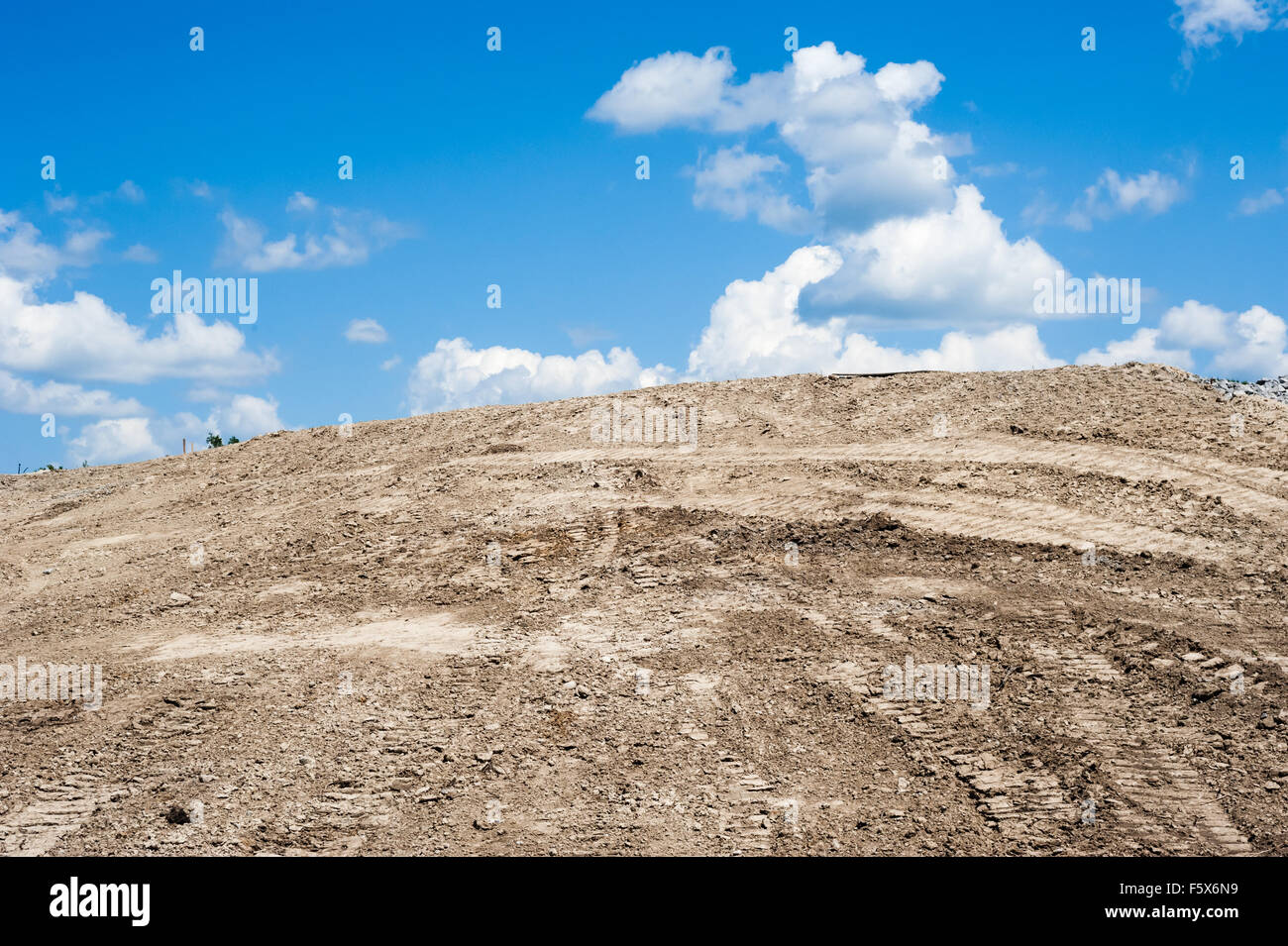 Monticule de terre de sable avec pneus et chenilles, se terminant à ciel bleu avec des nuages. Banque D'Images