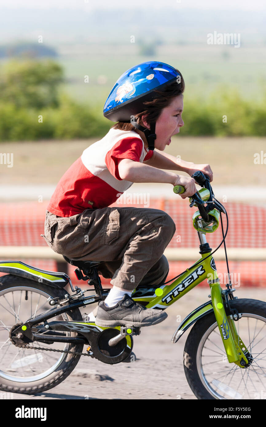 Vue latérale de Blancs 9 ans enfant, garçon, équitation, bicyclette d'enfant en vitesse avec enthousiaste de l'expression du visage. Le port de casque bleu et tee-shirt. Banque D'Images