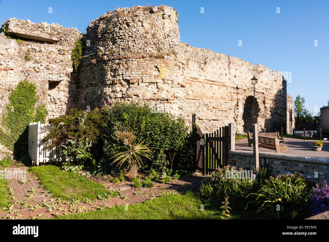 L'Angleterre. 4e siècle romain côte saxonne fort, château de Pevensey. East gateway avec tour de défense et des murs. Ciel bleu. Jardin en premier plan. Banque D'Images