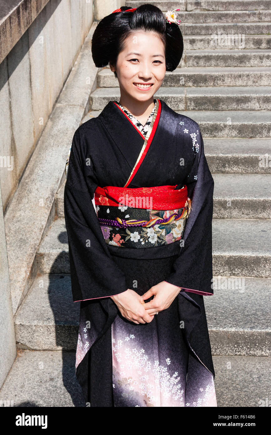 Le Japon, Kyoto. Femme mature, en kimono rouge avec ceinture obi, debout  dans la lumière du soleil sur les marches de pierre, souriant tout en se  posant. En face. Pas de contact