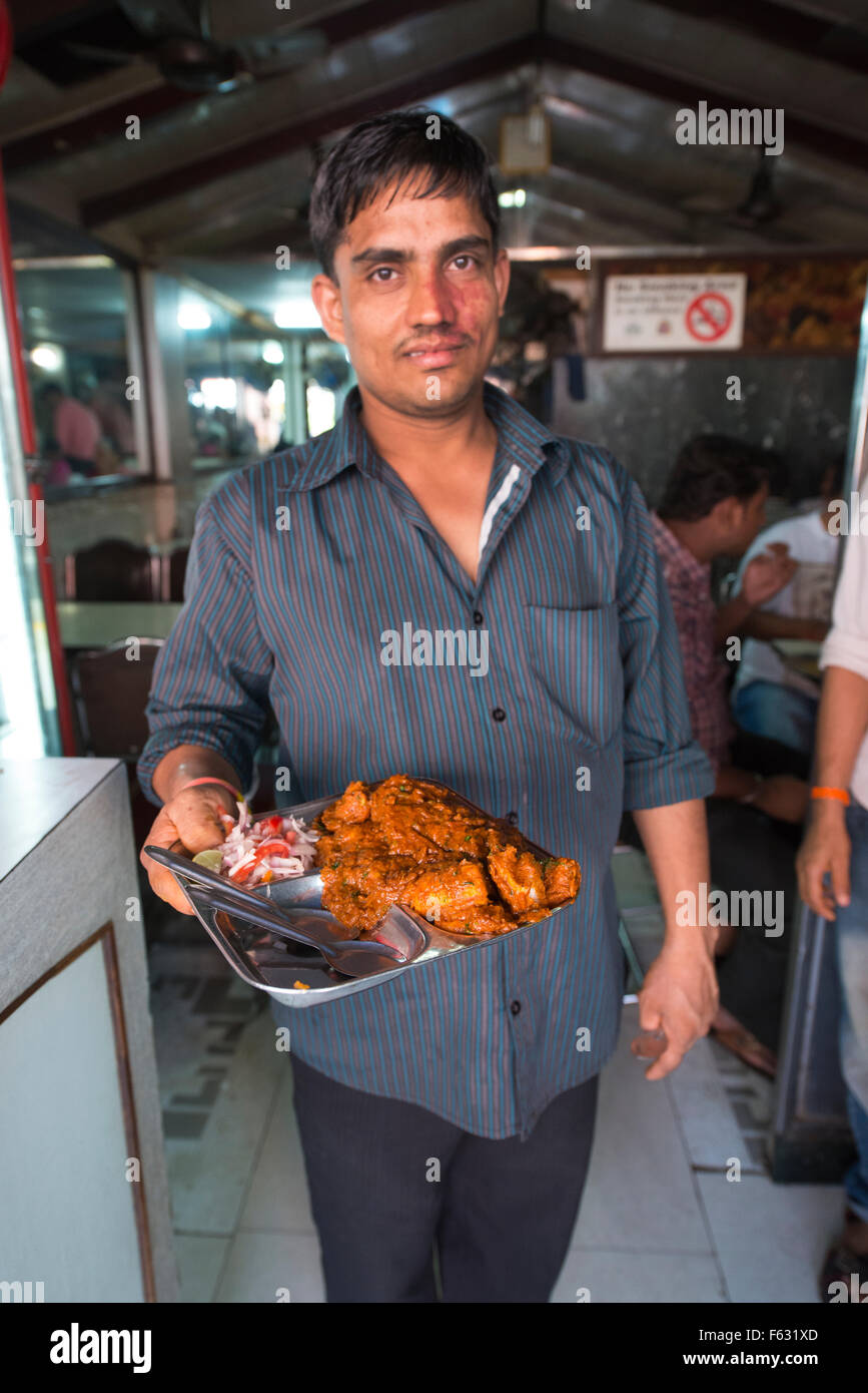 Un serveur qui sert un plat de curry dans un petit restaurant à Mumbai. Banque D'Images