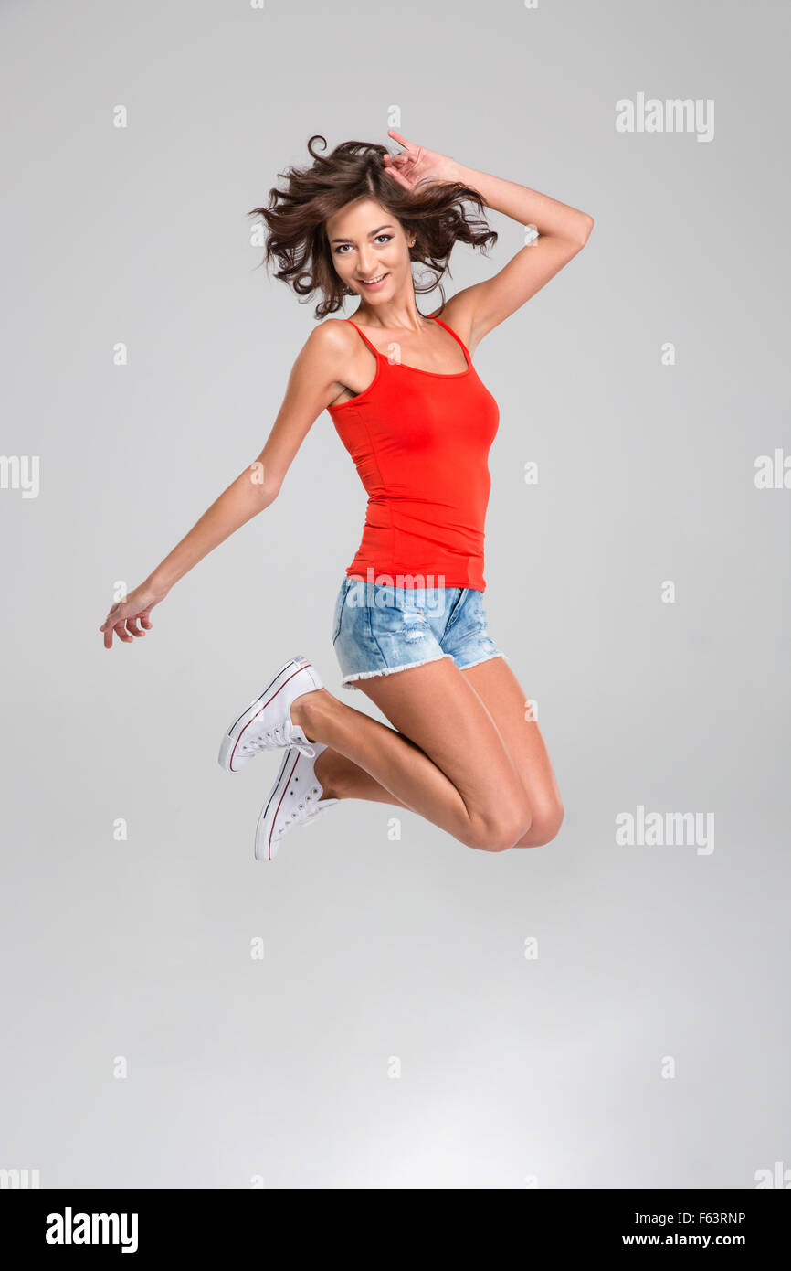 Jeune femme insouciante heureux bouclés à Red top, short jeans blanc et  sneackers jumping and smiling Photo Stock - Alamy
