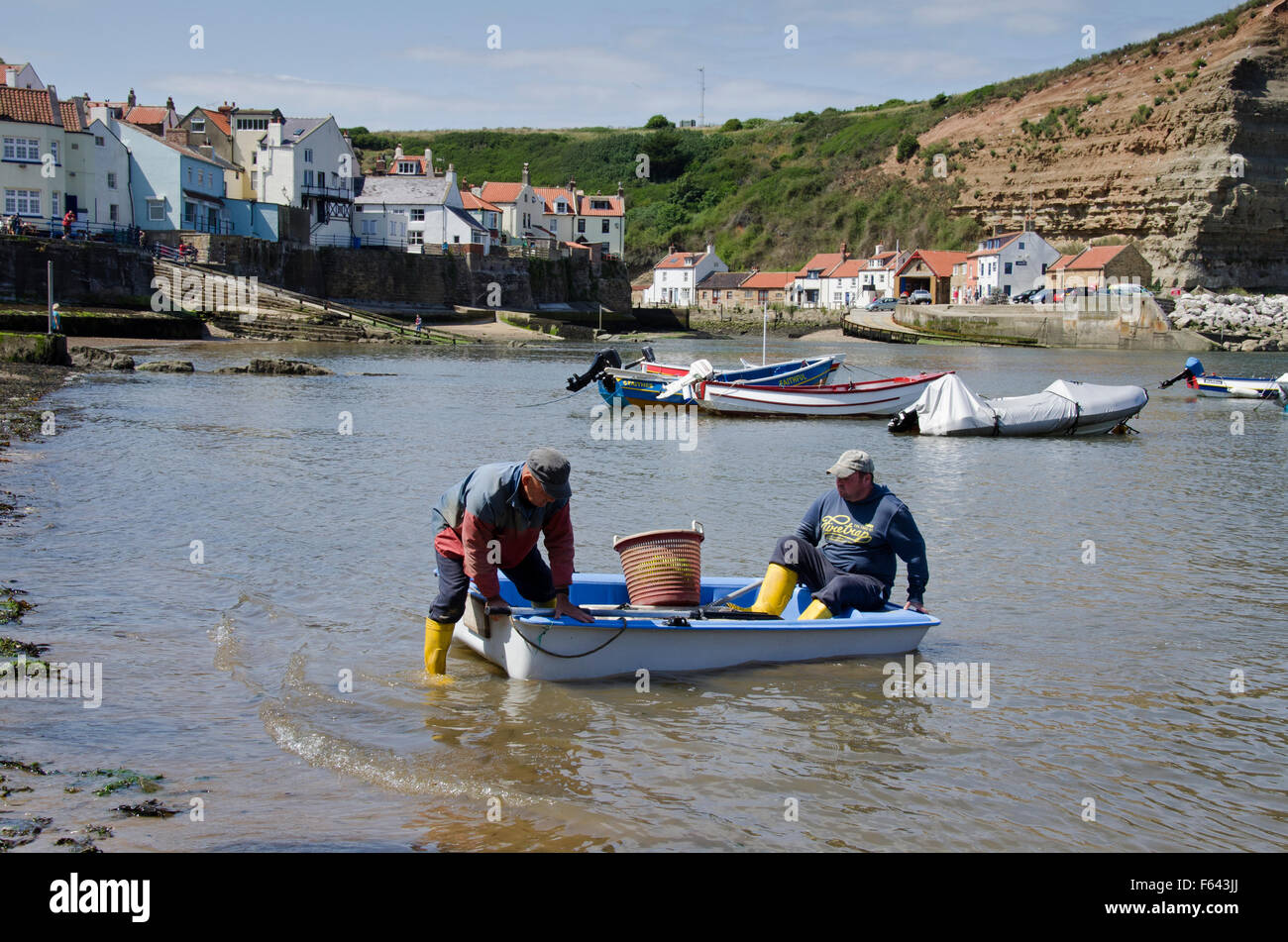 2 pêcheurs dans un petit bateau, débarquer leurs prises dans un seau sur le bord de la mer - journée ensoleillée, Harbour beach, Staithes' village, North Yorkshire, UK. Banque D'Images
