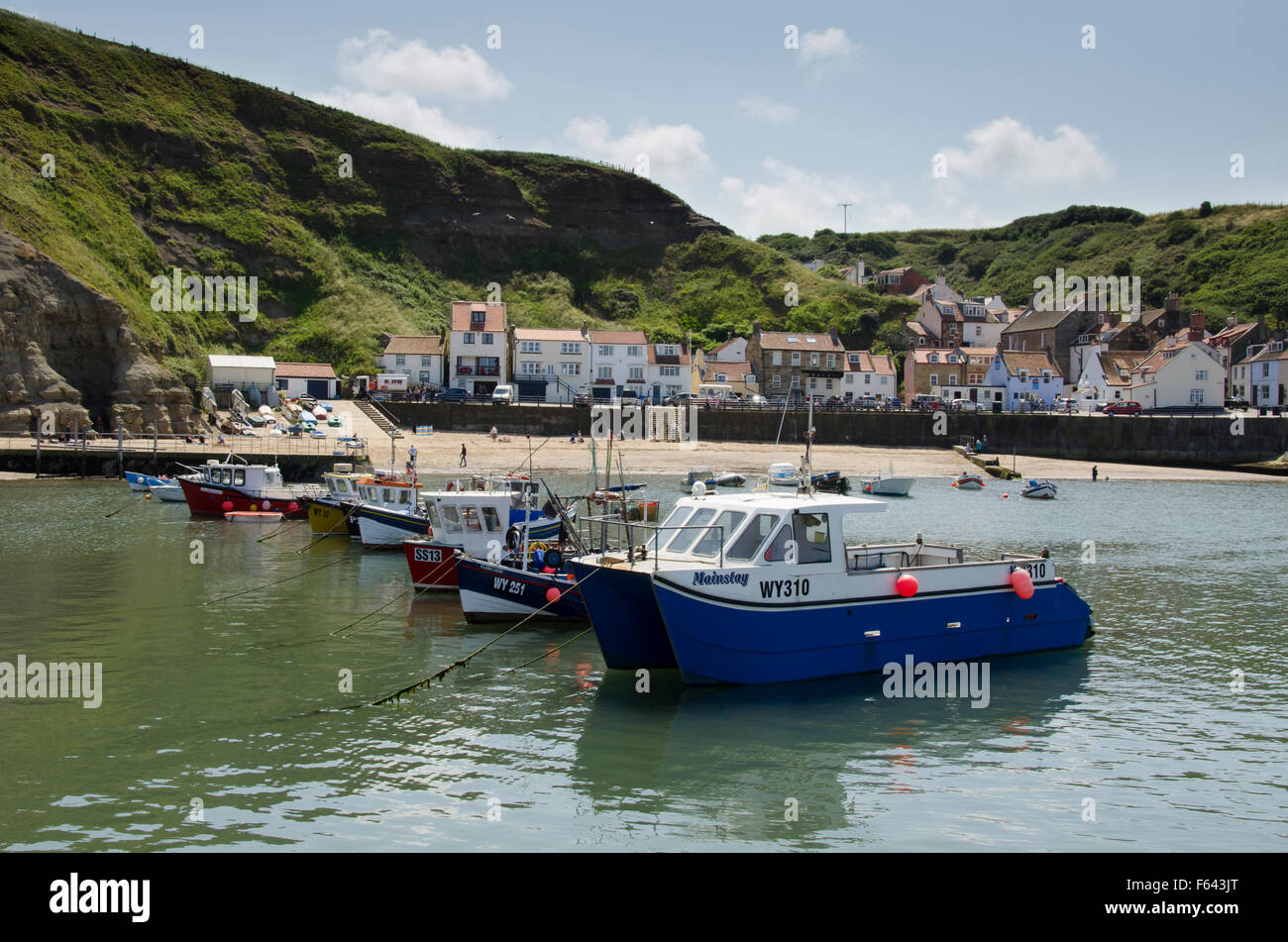 Sous le soleil d'été, les bateaux de pêche colorés sont amarrés dans le port de la mer, avec le pittoresque village de Staithes, North Yorkshire, UK, au-delà. Banque D'Images