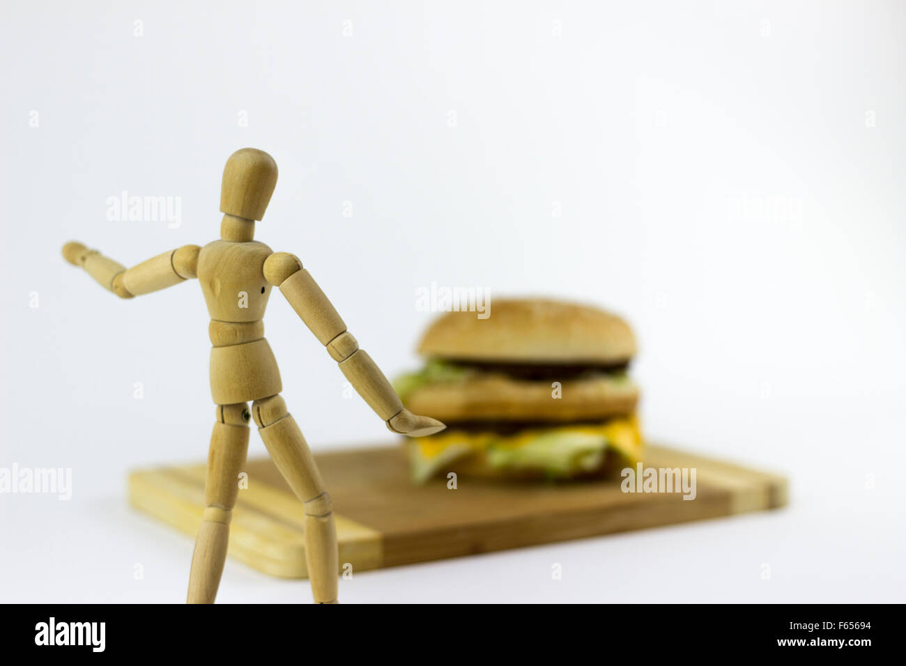 Une marionnette en bois à la recherche à un hambuger sur fond blanc Banque D'Images