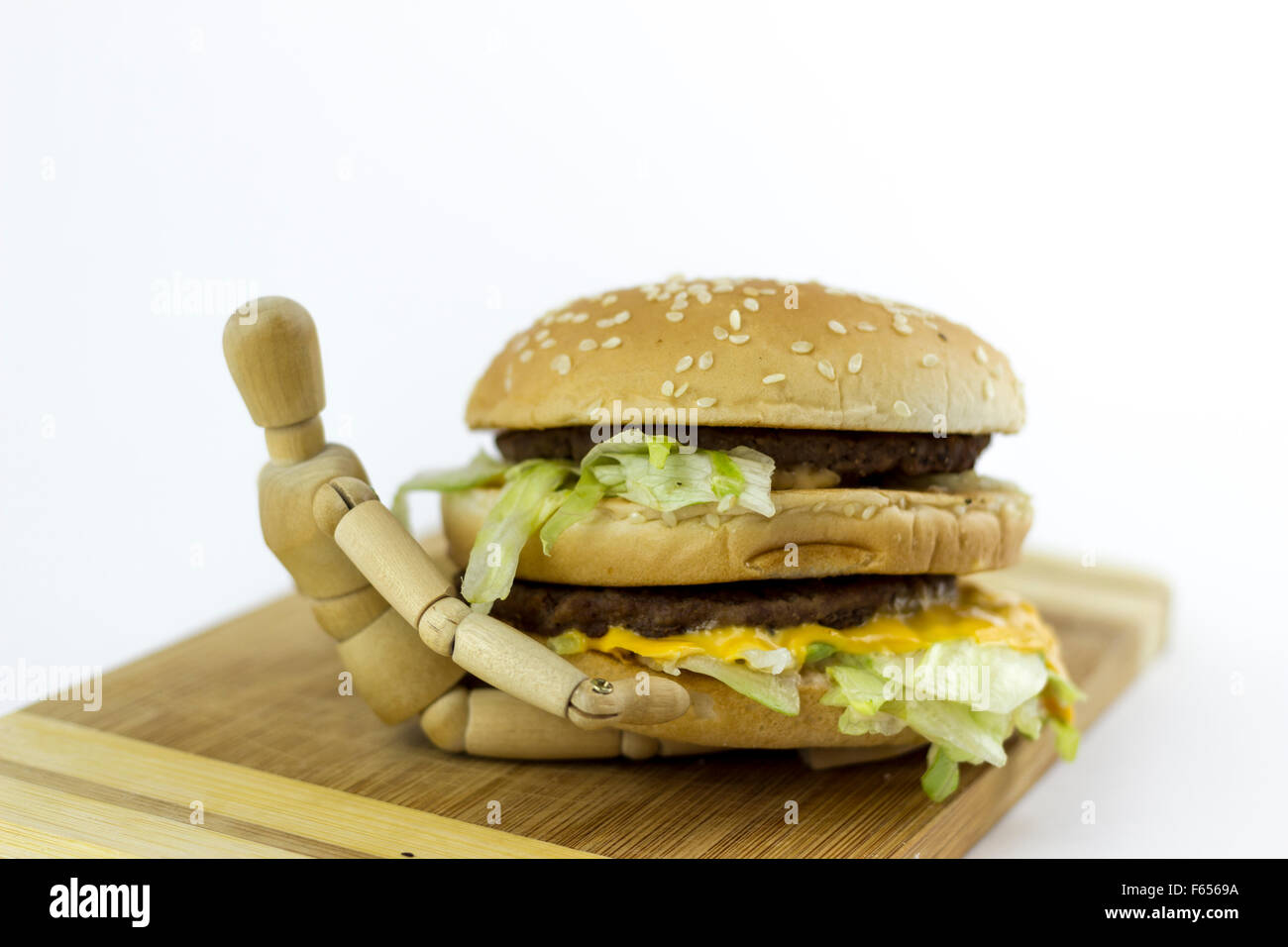 Poupée en bois debout sur une planche à découper sur un fond blanc, tenant un hamburger Banque D'Images