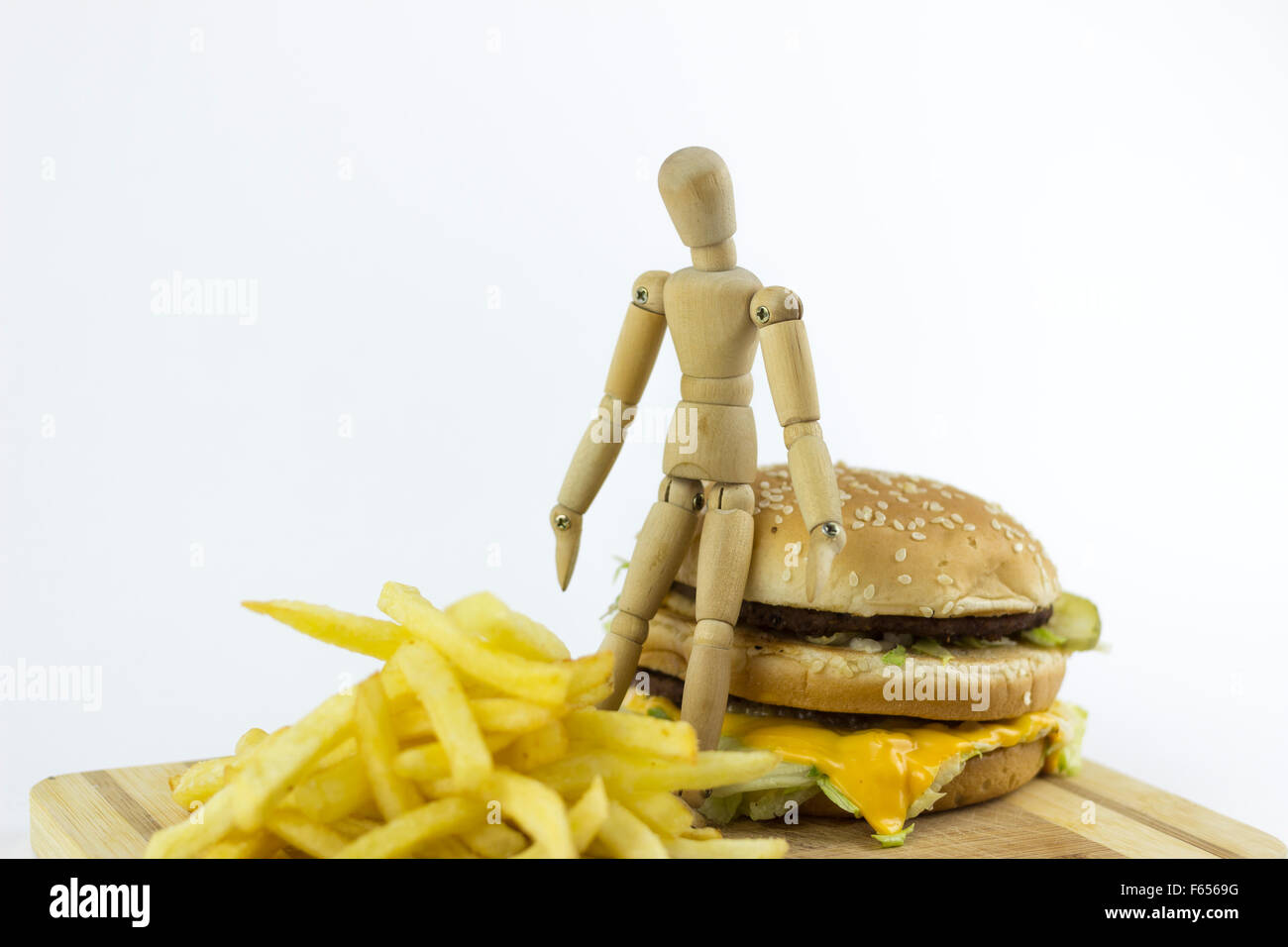 Poupée en bois debout sur un hamburger, examiner quelques frites Banque D'Images