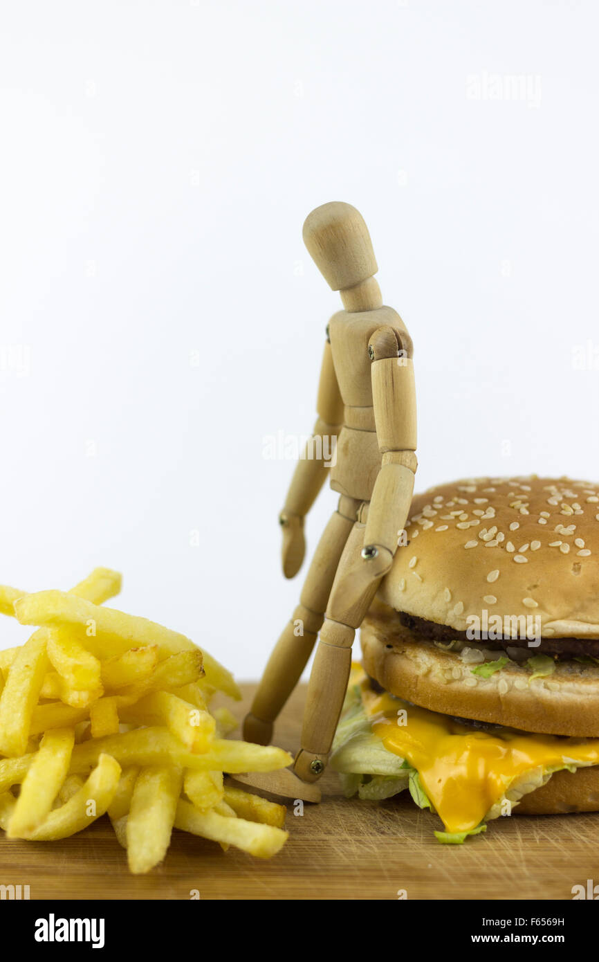 Poupée en bois debout sur un hamburger, examiner quelques frites Banque D'Images