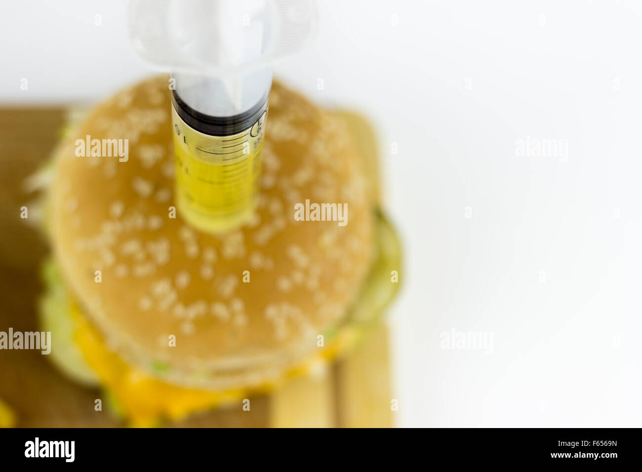 Liquide jaune puming seringue dans un hamburger, sur un fond blanc Banque D'Images