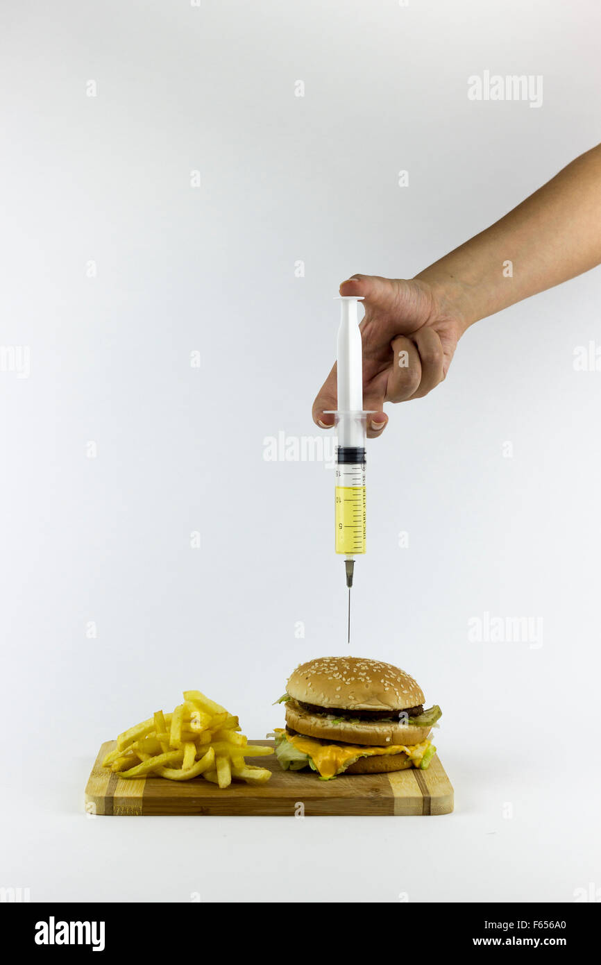 Pompage de liquides dans la main un hamburger avec une seringue, sur un fond blanc Banque D'Images