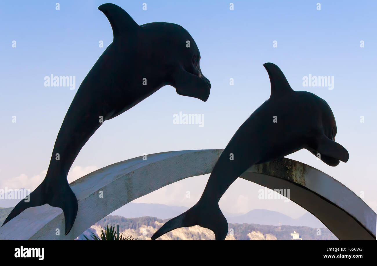Contre le ciel bleu sur le piédestal sont deux sculptures de dauphins. Dans la distance est un paysage montagneux. Banque D'Images
