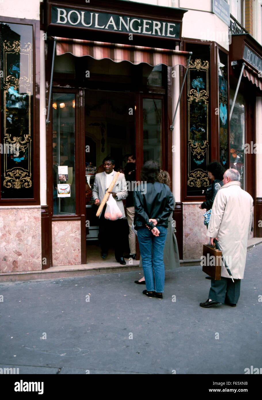 AJAXNETPHOTO. PARIS, FRANCE. - BOULANGERIE - UN HOMME AVEC UNE BAGUETTE EN PASSANT LES GENS faisant la queue pour acheter du pain À UNE BOULANGERIE - PAIN SHOP - SUR LA RUE DU FAUBOURG SAINT ANTOINE ET COIN DE LA RUE DES IMMEUBLLES INDUSTRIELS, 11eArr. Plus tard changé de façade cette décoration traditionnelle à gris neutre. photo:JONATHAN EASTLAND/AJAX REF:61401 2036 Banque D'Images