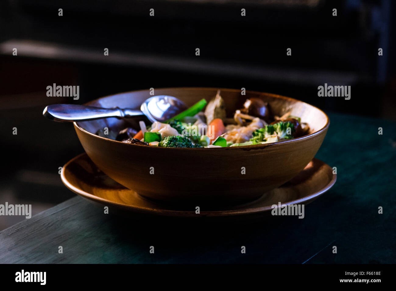 Vue de la soupe aux légumes ou ragoût dans une couleur brune ou tan bowl dans une plaque, sur un bleu verdâtre du grain du bois dans l'environnement rustique Banque D'Images