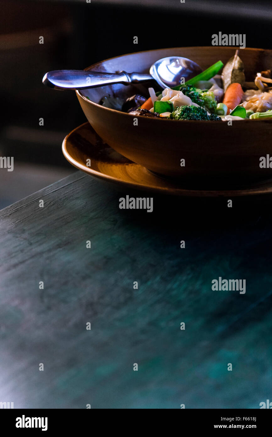 Vue de la soupe aux légumes ou ragoût dans une couleur brune ou tan bowl dans une plaque, sur un bleu verdâtre du grain du bois dans l'environnement rustique Banque D'Images