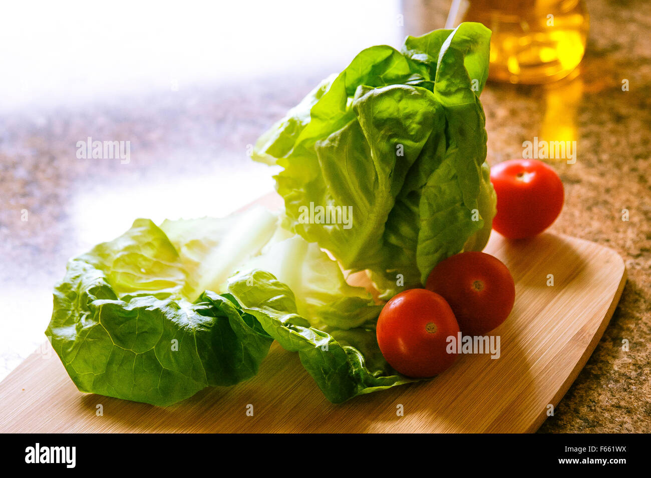 Laitue, tomate et oignon vert, planche à découper en bambou, et de l'huile sur le comptoir de granit, rétroéclairé Banque D'Images