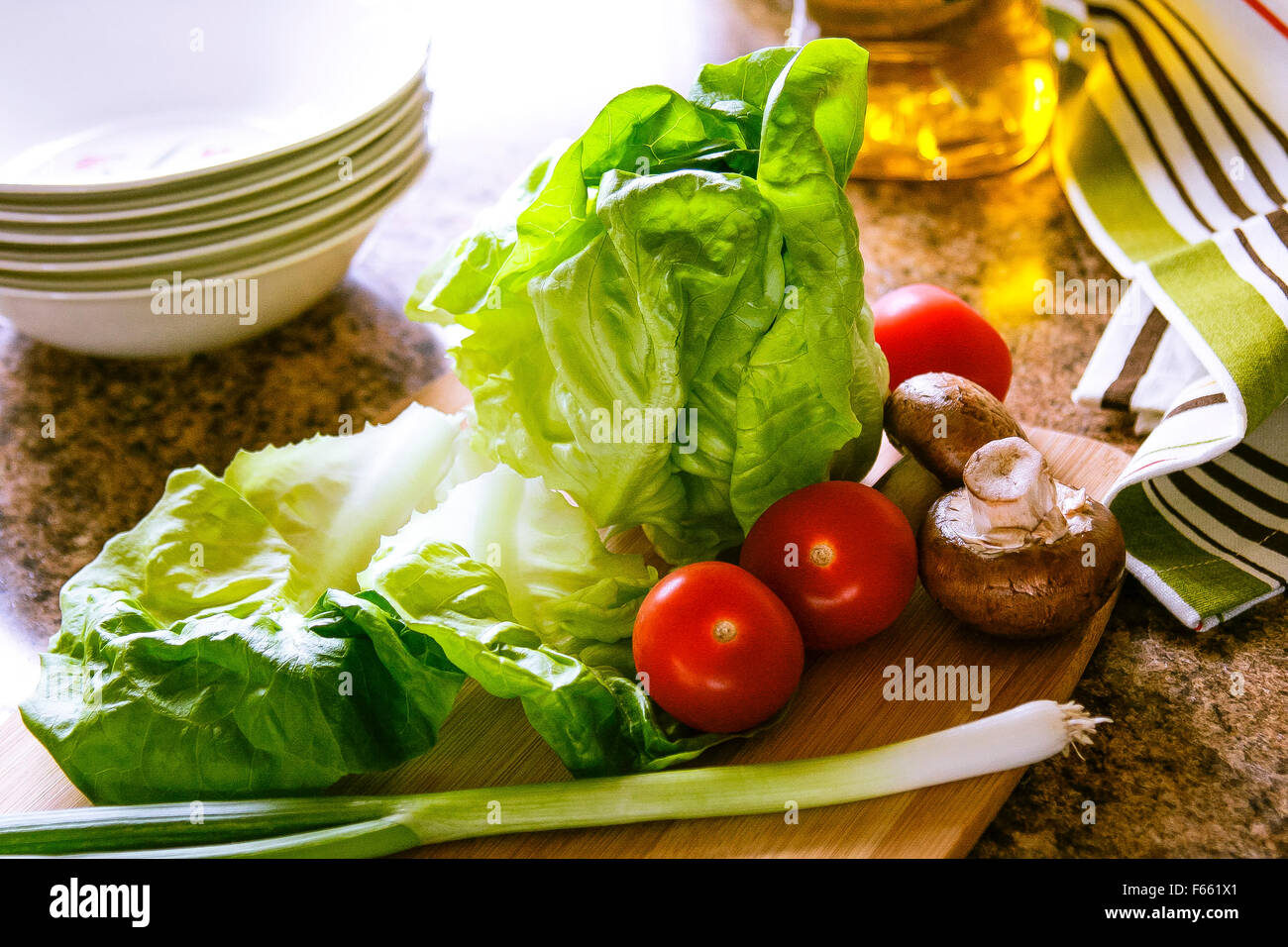 Laitue, tomate et oignon vert, planche à découper en bambou, un chiffon et de l'huile sur le comptoir de granit, rétroéclairé Banque D'Images