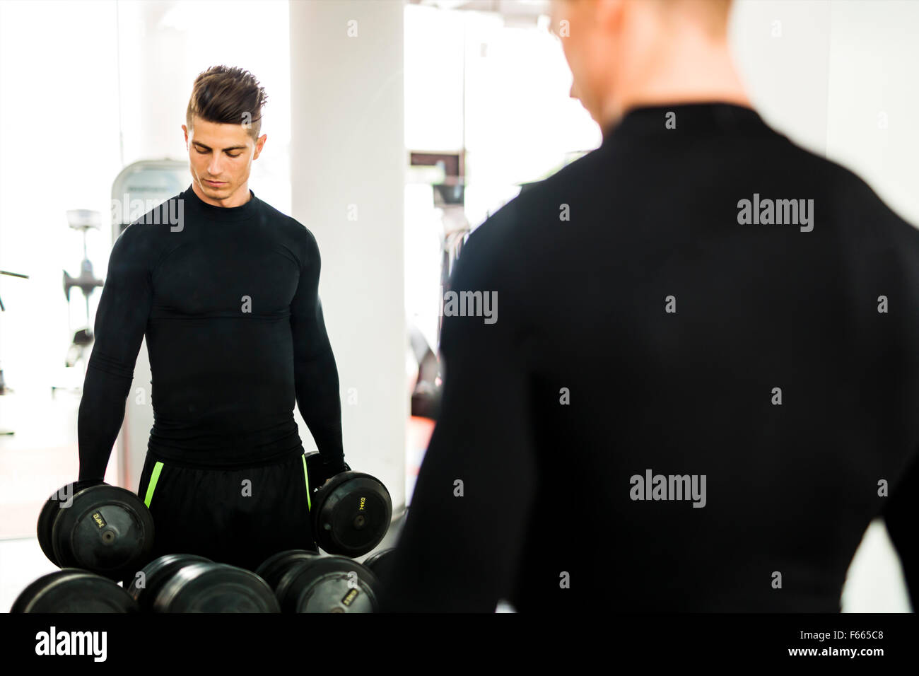 Jeune homme musclé de vous entraîner dans une salle de sport et de lever des poids avec son reflet dans un miroir Banque D'Images