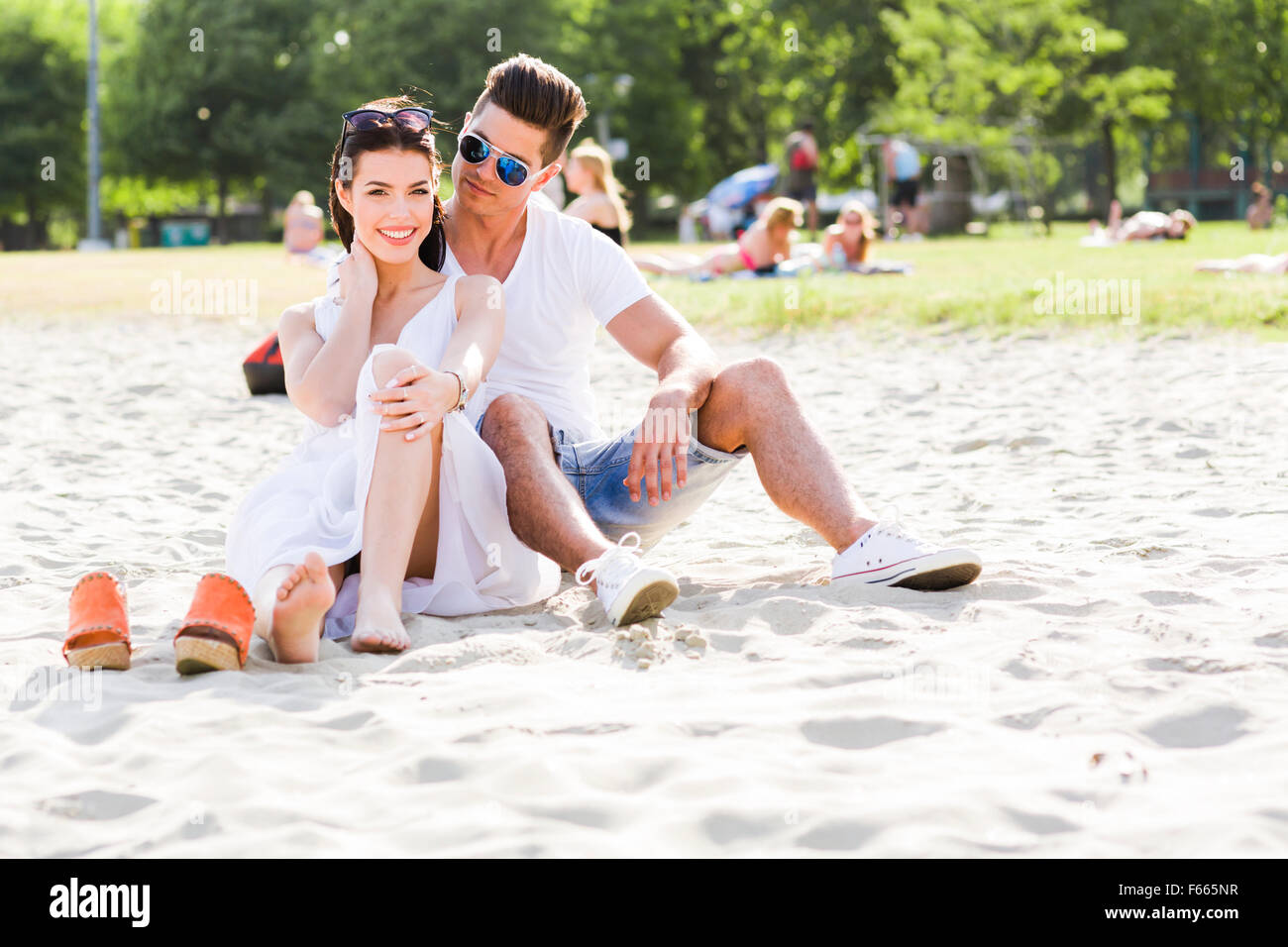 Couple amoureux assis à une plage de sable fin et souriant Banque D'Images
