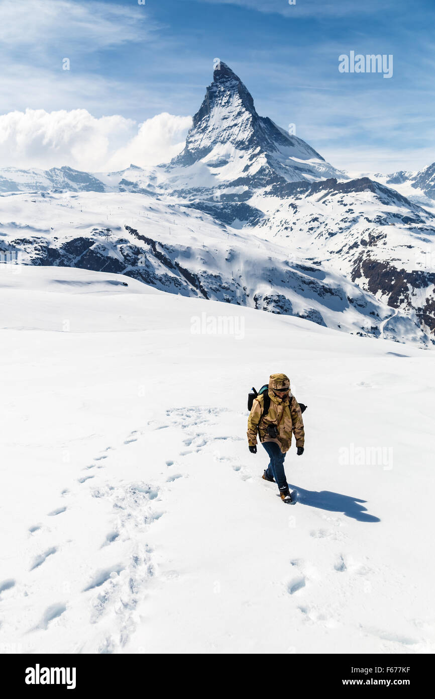 Un homme en manteau d'hiver camouflage marche sur la neige avec l'arrière-plan de Cervin. Banque D'Images