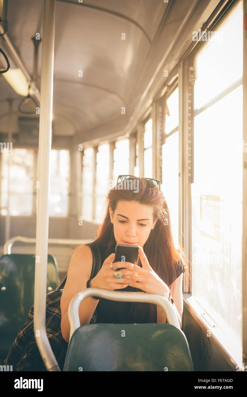 La moitié de la longueur d'une belle jeune femme caucasienne cheveux brun rougeâtre à l'aide d'un smartphone sur un tram - technologie, réseau social, concept de communication - à l'écran vers le bas Banque D'Images