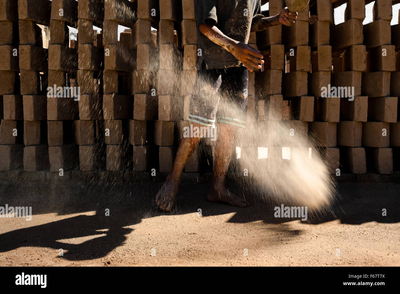 Brian, un garçon, jette du sable sur le terrain afin de le préparer pour briques crues à une briqueterie dans Istahua, El Salvador. Banque D'Images