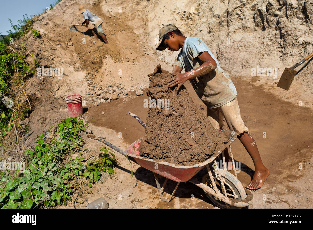 Moisés, un garçon, brouette remplit avec de l'argile pour la fabrication de briques à une briqueterie dans Istahua, El Salvador. Banque D'Images