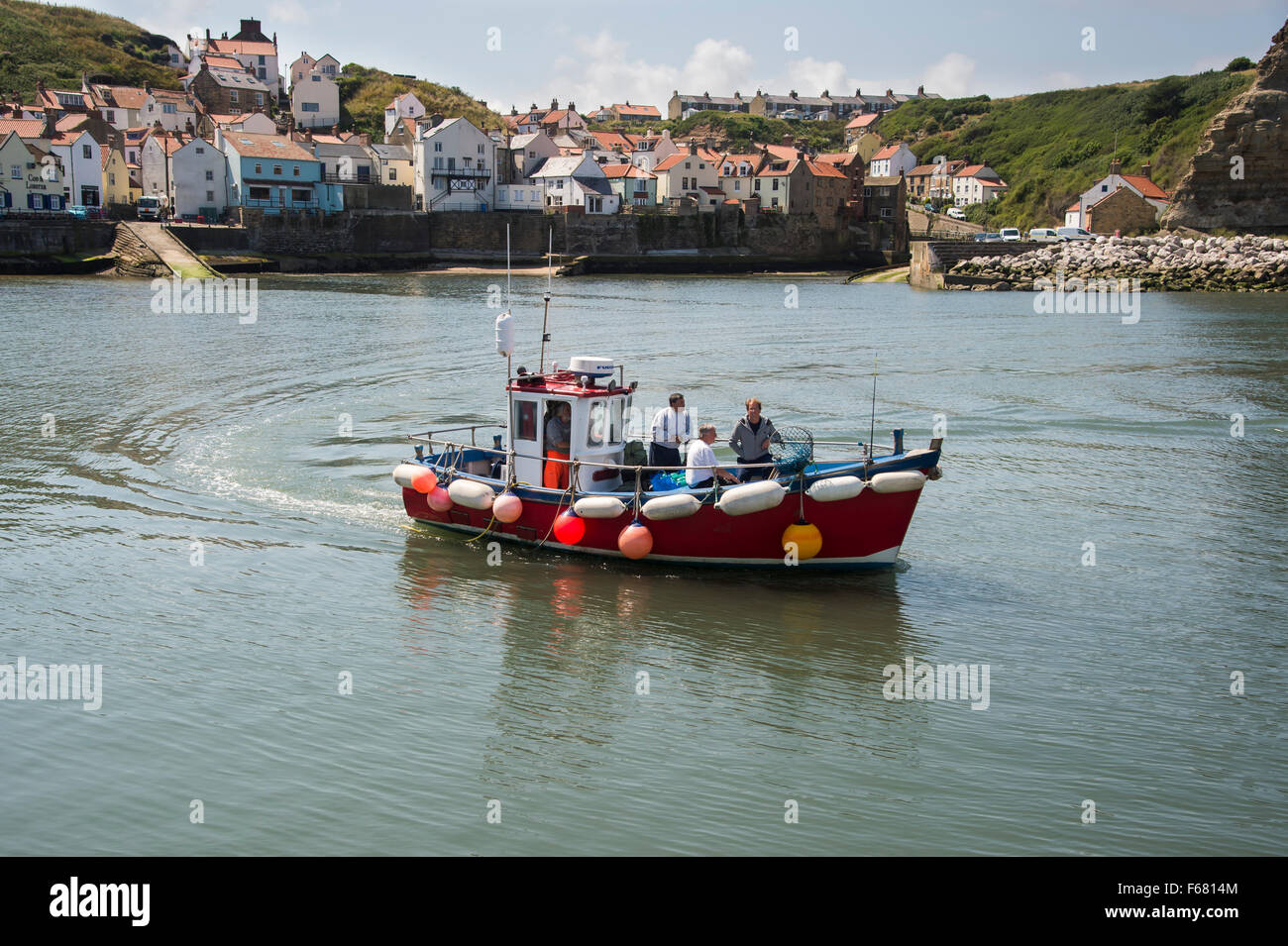 Journée d'été ensoleillée et quatre hommes sur un bateau de pêche en mer, de quitter le port et pittoresque, village côtier de Staithes, North Yorkshire, Angleterre, Royaume-Uni. Banque D'Images