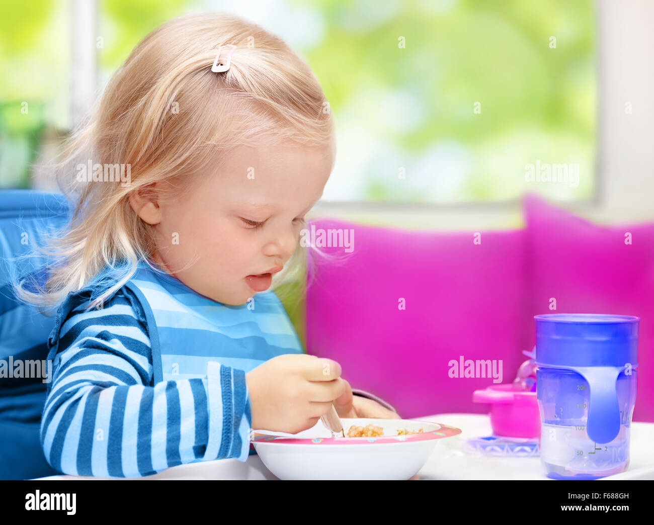 Mignon petit blond bébé fille assise sur la cuisine à la maison et prendre le petit-déjeuner, une saine nutrition de l'enfant, heureux de l'enfant sans souci Banque D'Images