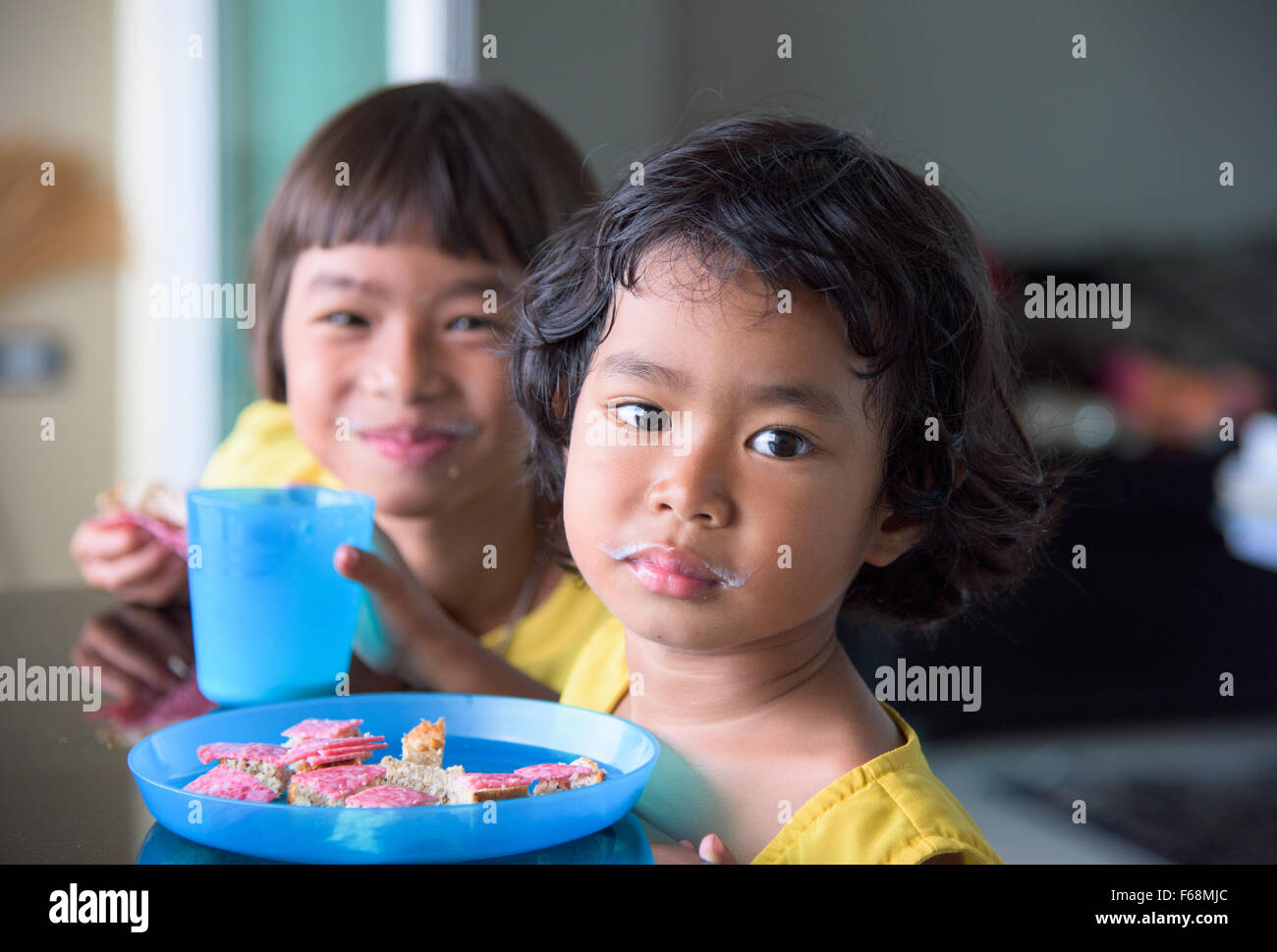 Deux filles Thai, 3 et 7 ans, la consommation de lait et de manger du pain avec du salami. Les deux grils ont une moustache de lait visible. Banque D'Images