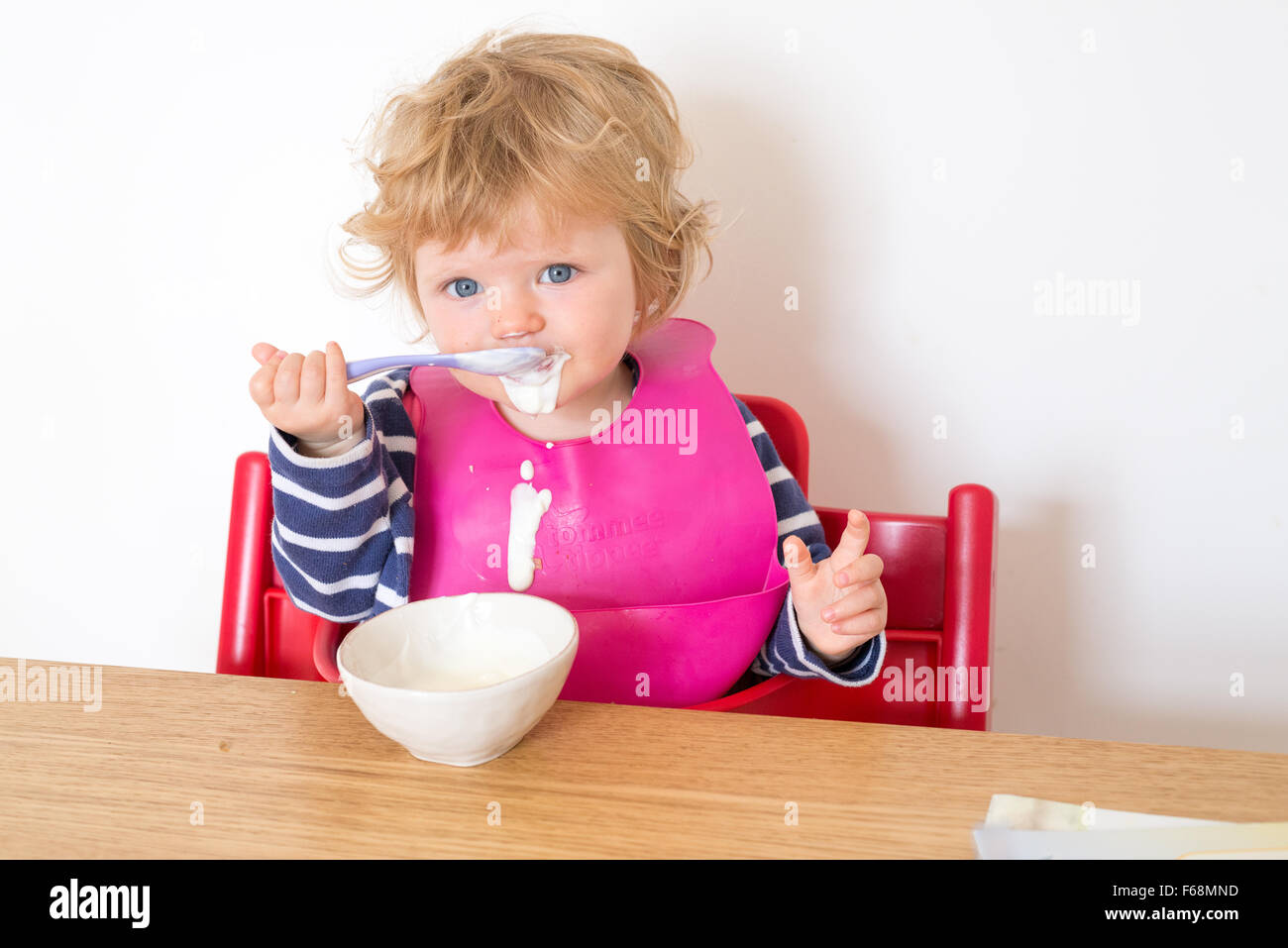 Un an bébé qui mange son yaourt avec une cuillère, salissent en Angleterre, Royaume-Uni Banque D'Images