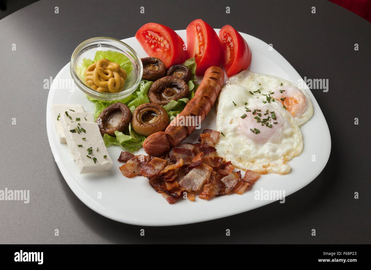 Petit-déjeuner servi sur une plaque blanche, oeufs, fromage, bacon, champignons, tomates Banque D'Images