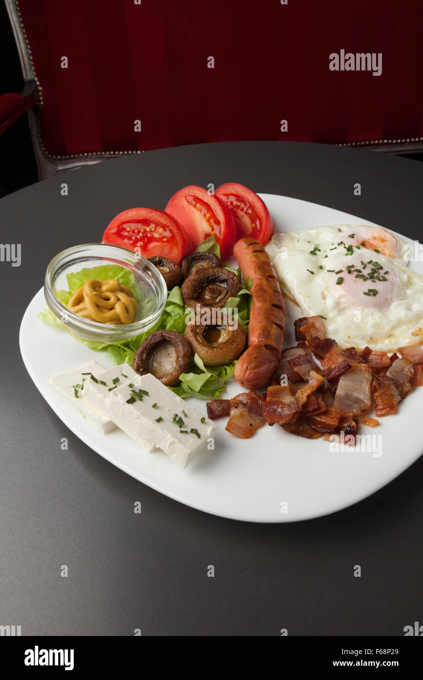 Petit-déjeuner servi sur une plaque blanche, oeufs, fromage, bacon, champignons, tomates Banque D'Images