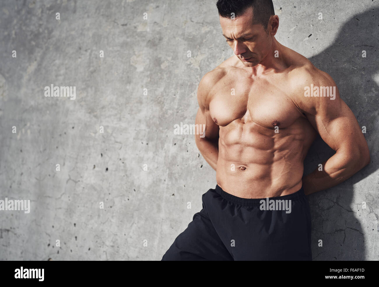 Close up image de l'homme en short se détendre après entraînement sur fond gris. Corps de l'homme musclé avec la sueur. Image avec copyspace Banque D'Images