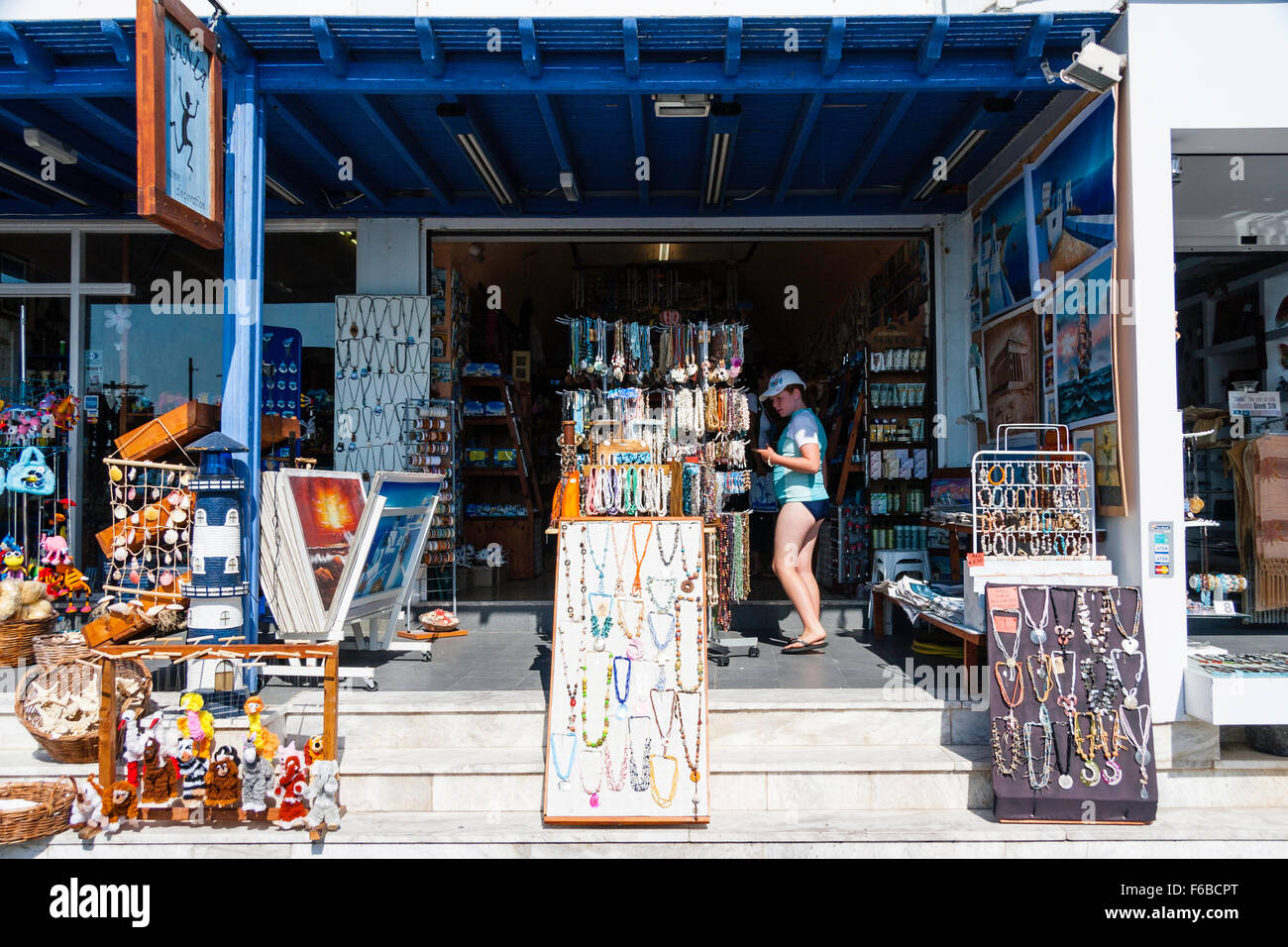 Santorin, Théra. Kamari. Ouvrir Mini market store, à l'extérieur, sur les marches, divers produits et des présentoirs de cartes postales, touriste choisissant collier. Banque D'Images