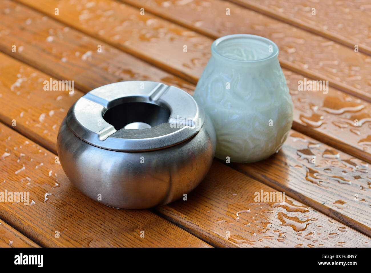 Un cendrier de métal et un lustre pour une bougie sur la table à l'extérieur couverts par gouttes de pluie Banque D'Images
