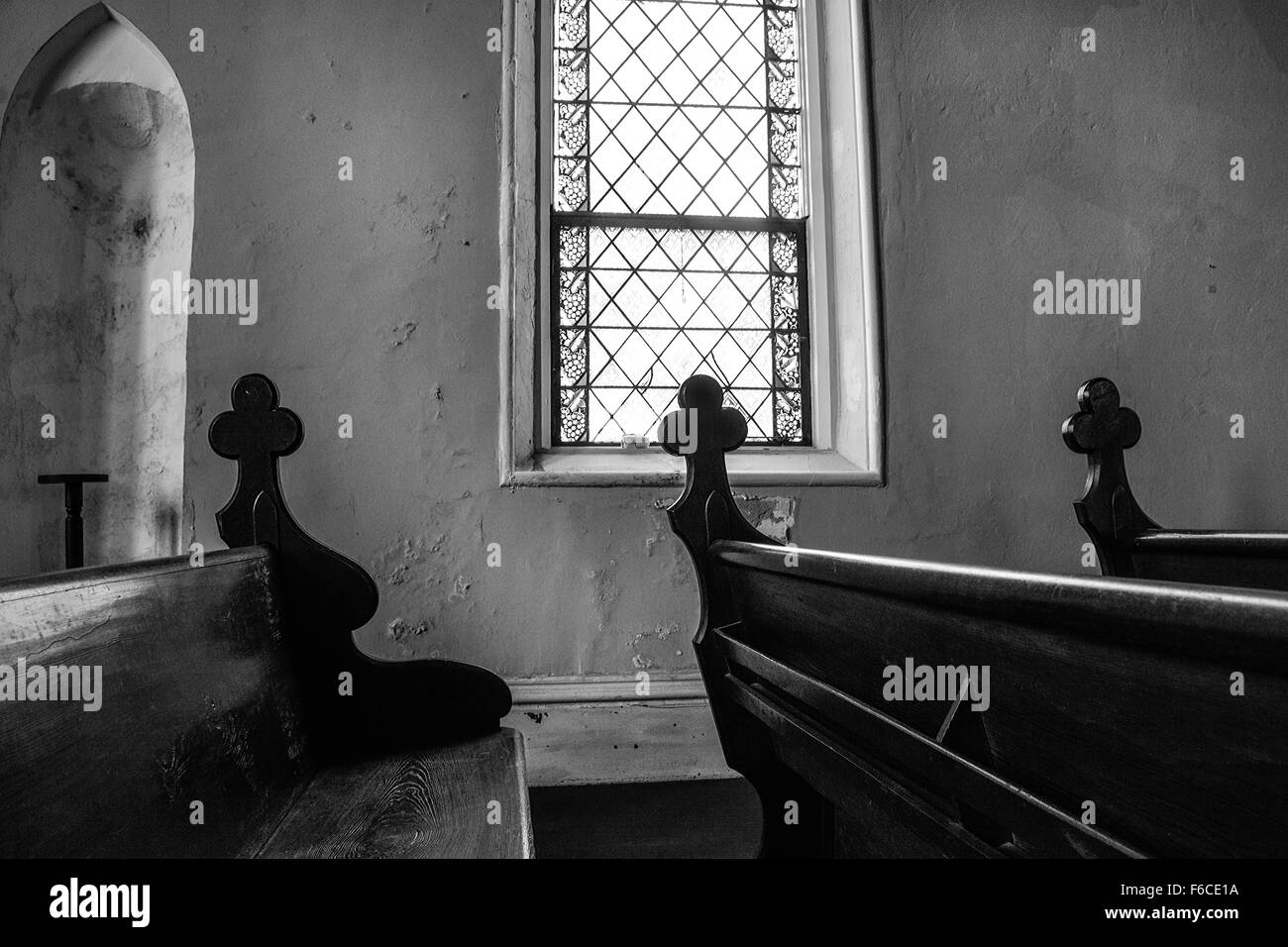 Une pièce faiblement éclairée de l'intérieur de l'église un vitrail fenêtre avec croix sculptées décorativement mis sur les extrémités de chaque art pew en bois Banque D'Images