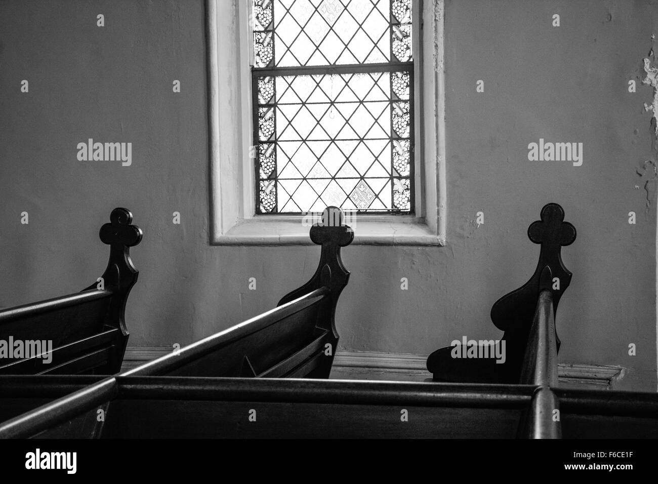 Une pièce faiblement éclairée de l'intérieur de l'église un vitrail fenêtre avec croix sculptées décorativement mis sur les extrémités de chaque art pew en bois Banque D'Images